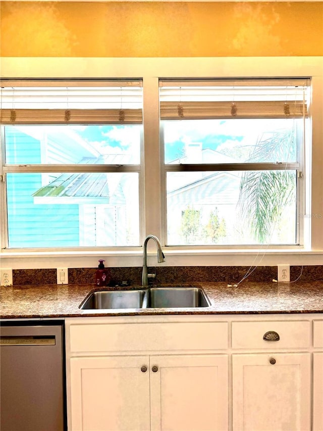 kitchen featuring stainless steel dishwasher, dark stone countertops, a sink, and white cabinetry