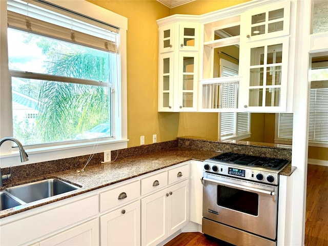 kitchen featuring stainless steel range with gas stovetop, a sink, white cabinets, dark wood finished floors, and glass insert cabinets