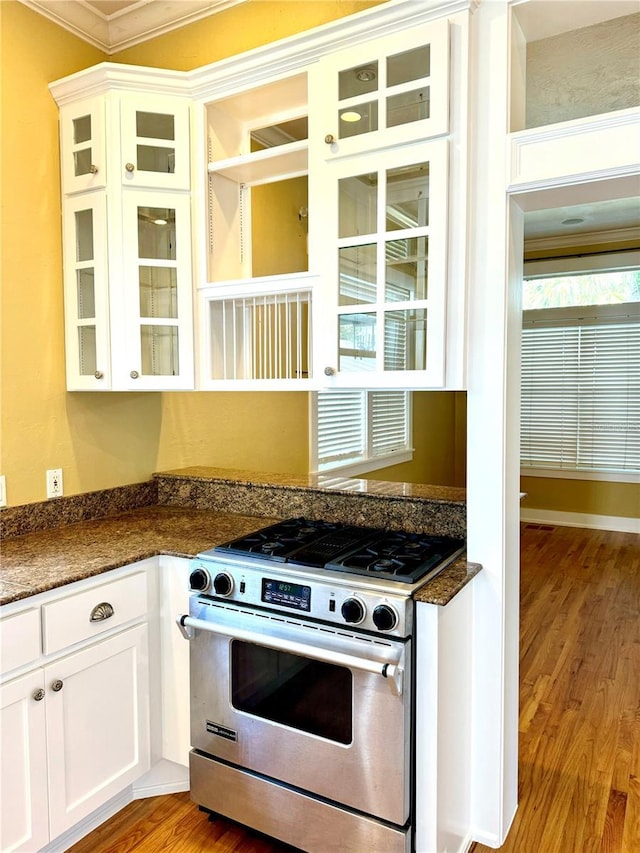 kitchen featuring white cabinets, ornamental molding, stainless steel gas stove, light wood finished floors, and glass insert cabinets