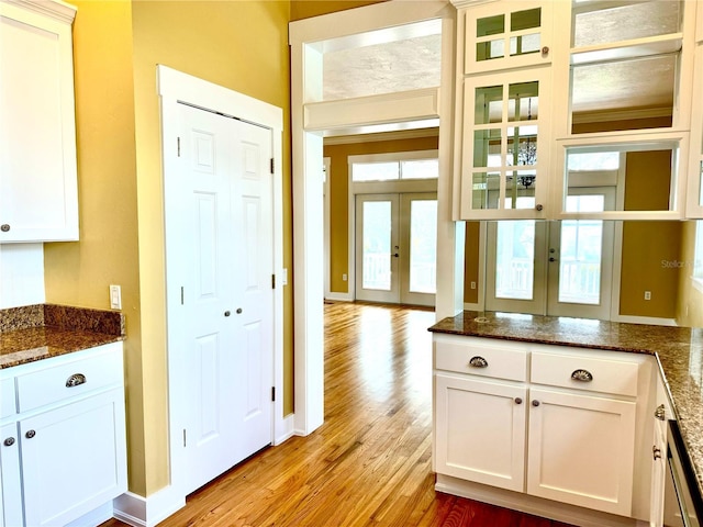 kitchen with glass insert cabinets, dark stone countertops, french doors, light wood-style floors, and white cabinetry