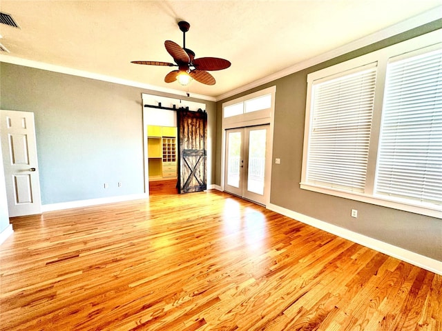 unfurnished room featuring french doors, crown molding, a barn door, light wood-style floors, and baseboards