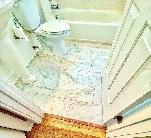 full bathroom featuring a washtub, marble finish floor, and toilet