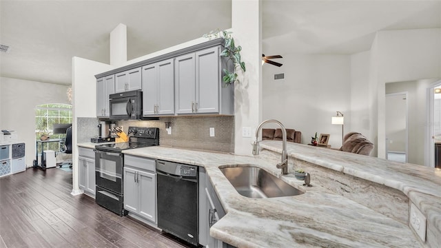 kitchen with light stone counters, dark wood-style flooring, decorative backsplash, a sink, and black appliances