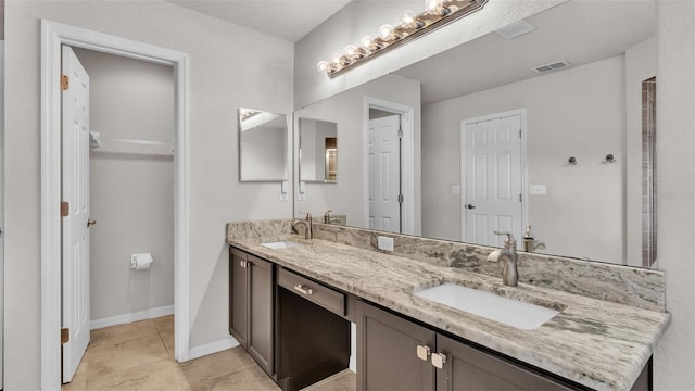 full bath with double vanity, a sink, visible vents, and baseboards