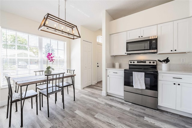 kitchen with light wood finished floors, light countertops, appliances with stainless steel finishes, an inviting chandelier, and white cabinets