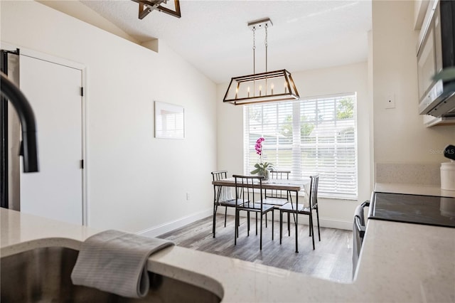 dining space with an inviting chandelier, baseboards, lofted ceiling, and wood finished floors