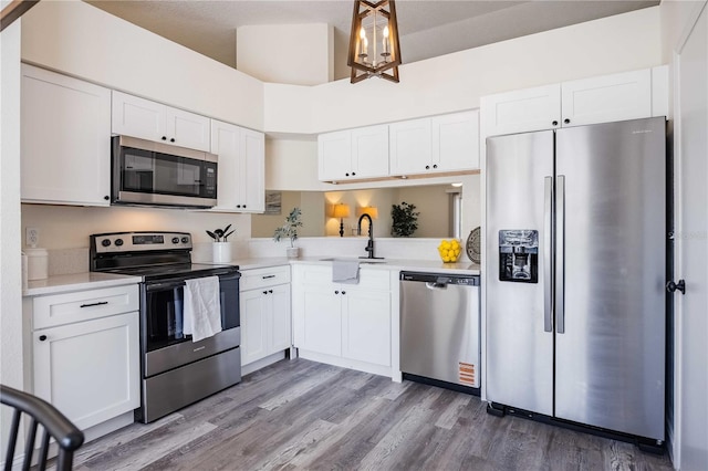 kitchen with light countertops, stainless steel appliances, wood finished floors, white cabinetry, and a sink