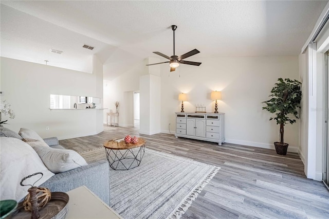 living area with visible vents, baseboards, vaulted ceiling, wood finished floors, and a ceiling fan