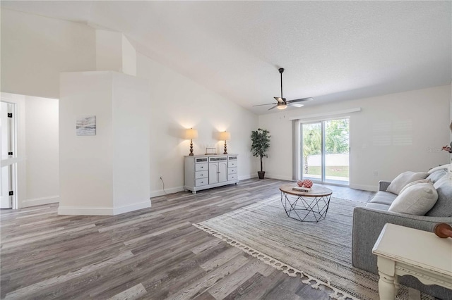 living room with lofted ceiling, a textured ceiling, wood finished floors, baseboards, and ceiling fan