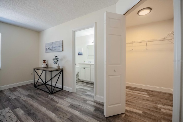 hallway with a sink, wood finished floors, baseboards, and a textured ceiling