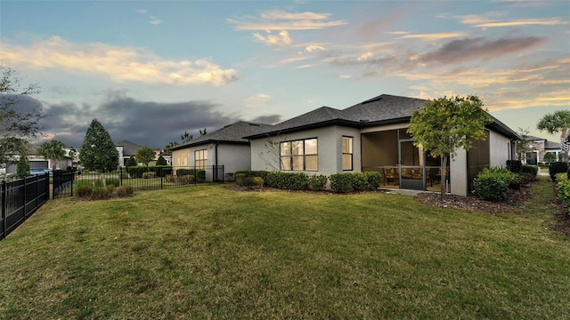 property exterior at dusk with a sunroom, a fenced backyard, a lawn, and stucco siding