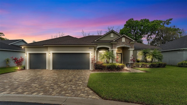 ranch-style home with stucco siding, a lawn, decorative driveway, a shingled roof, and a garage