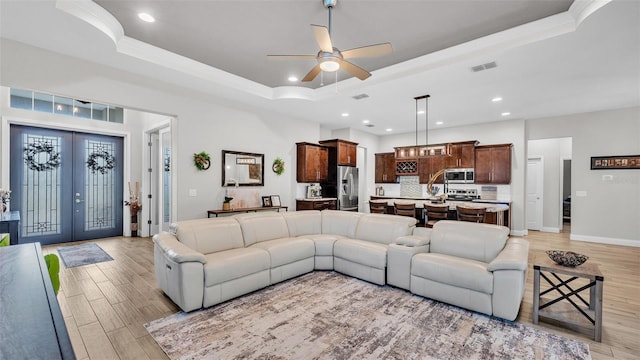 living room with recessed lighting, french doors, a raised ceiling, and light wood finished floors