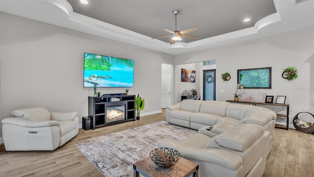 living area featuring a glass covered fireplace, a raised ceiling, and light wood-style floors