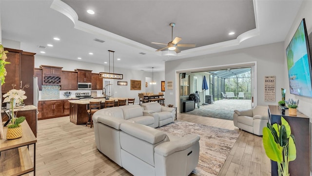 living room with recessed lighting, a tray ceiling, visible vents, and light wood-style flooring