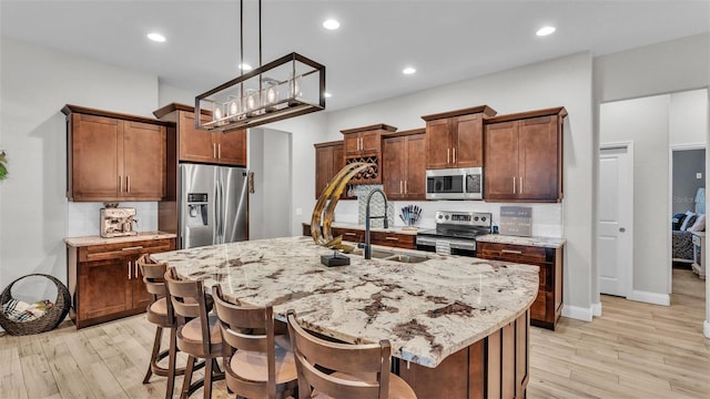 kitchen featuring a sink, light stone countertops, appliances with stainless steel finishes, and light wood finished floors