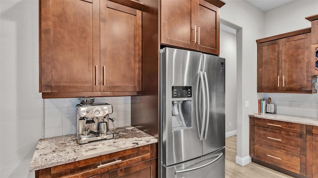 kitchen with backsplash, stainless steel fridge, light wood finished floors, and light stone countertops