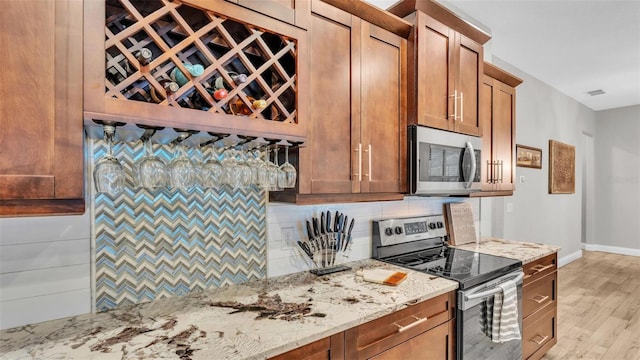 kitchen featuring light stone countertops, visible vents, light wood-style flooring, stainless steel appliances, and decorative backsplash