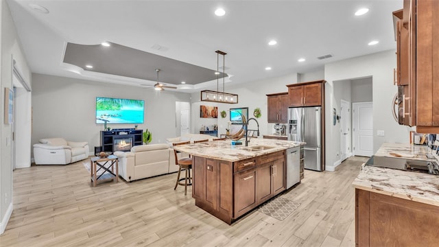 kitchen featuring open floor plan, a breakfast bar area, stainless steel appliances, a raised ceiling, and a sink