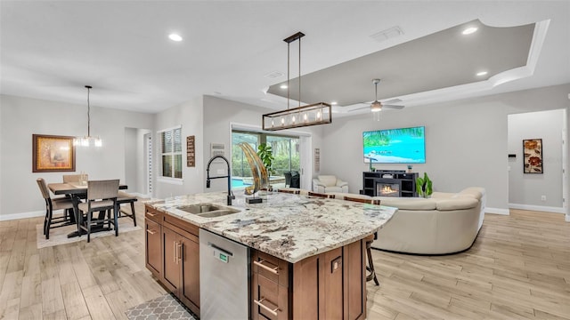 kitchen featuring a sink, light wood-type flooring, light stone countertops, and stainless steel dishwasher