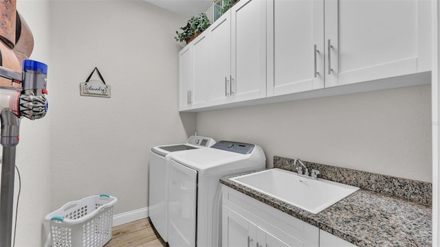 clothes washing area featuring light wood-type flooring, a sink, cabinet space, baseboards, and washing machine and clothes dryer