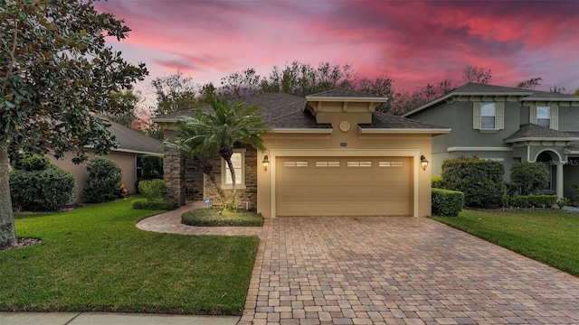 view of front of house with decorative driveway, an attached garage, a lawn, and stucco siding