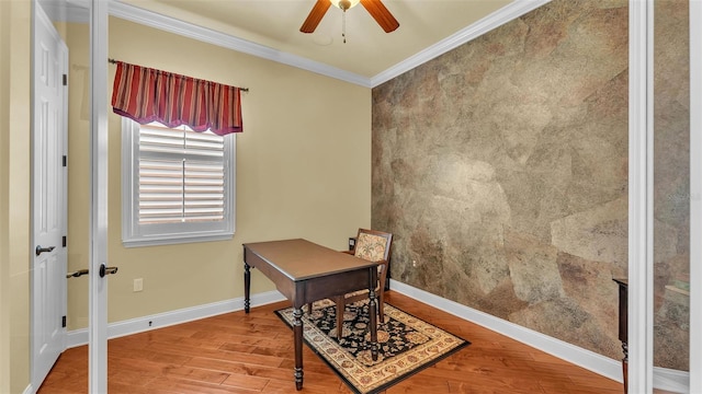 home office featuring baseboards, a ceiling fan, an accent wall, wood finished floors, and crown molding