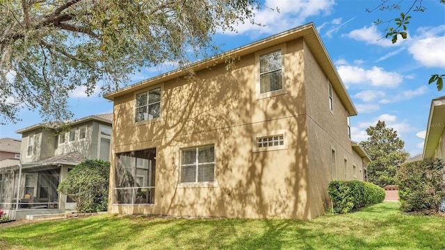 rear view of property with a sunroom, a lawn, and stucco siding