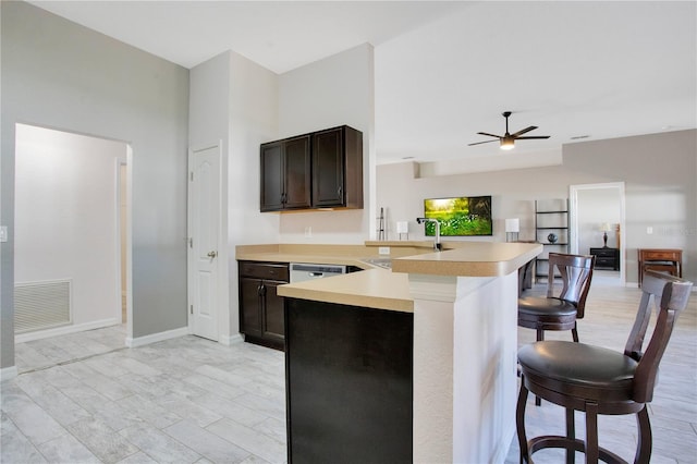 kitchen featuring visible vents, a breakfast bar, a sink, a peninsula, and light countertops