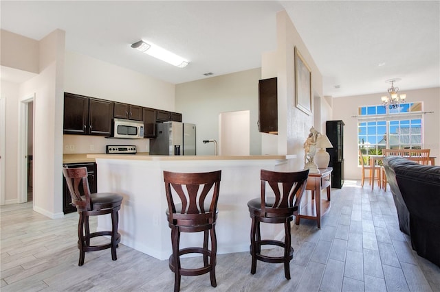 kitchen featuring light wood finished floors, dark brown cabinetry, appliances with stainless steel finishes, and a breakfast bar area