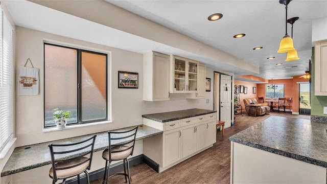 kitchen with dark wood finished floors, dark countertops, glass insert cabinets, hanging light fixtures, and recessed lighting