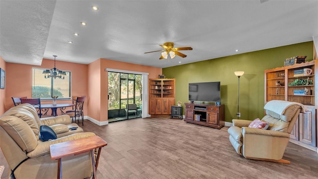 living room with ceiling fan with notable chandelier, baseboards, wood finished floors, and recessed lighting