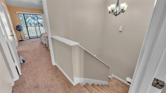 hall with carpet, baseboards, a notable chandelier, and an upstairs landing