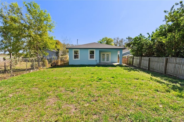 rear view of property featuring a lawn, french doors, a fenced backyard, and stucco siding