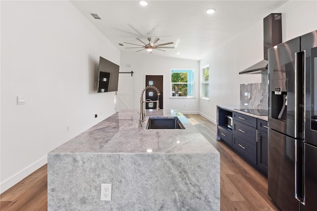 kitchen with a sink, wood finished floors, stainless steel appliances, a barn door, and wall chimney exhaust hood