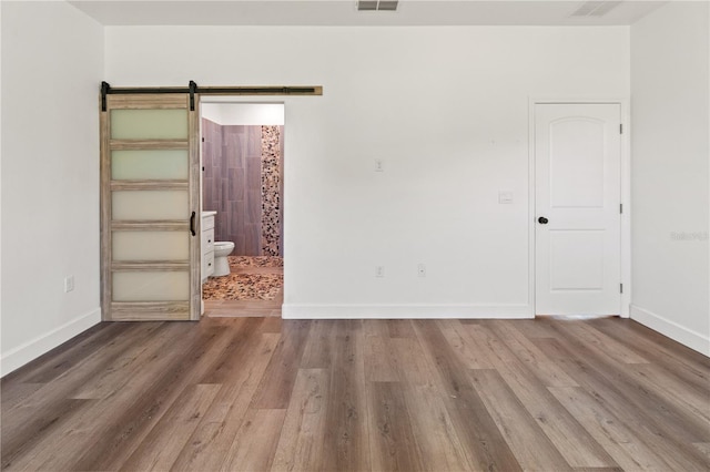 unfurnished room with baseboards, a barn door, and wood finished floors