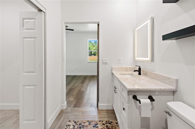 bathroom with toilet, vanity, baseboards, and wood finished floors