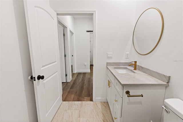 half bath featuring vanity, toilet, wood finished floors, and baseboards