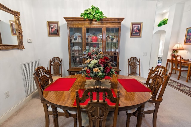 carpeted dining area with visible vents and arched walkways