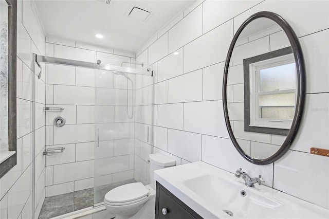 full bathroom featuring toilet, tiled shower, vanity, and tile walls