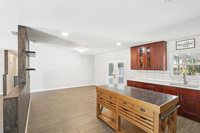 kitchen featuring reddish brown cabinets, tasteful backsplash, light wood-style flooring, and a sink