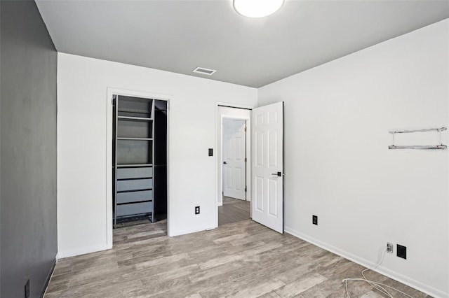 unfurnished bedroom with baseboards, a closet, visible vents, and wood finished floors