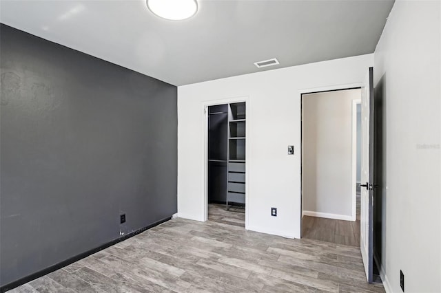 unfurnished bedroom featuring a closet, visible vents, a spacious closet, and wood finished floors