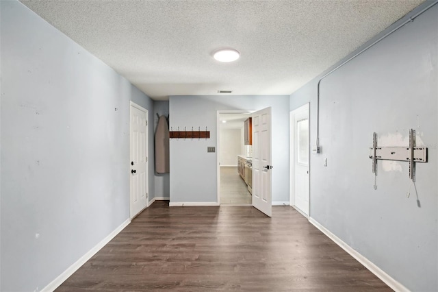 interior space with a textured ceiling, dark wood-type flooring, visible vents, and baseboards