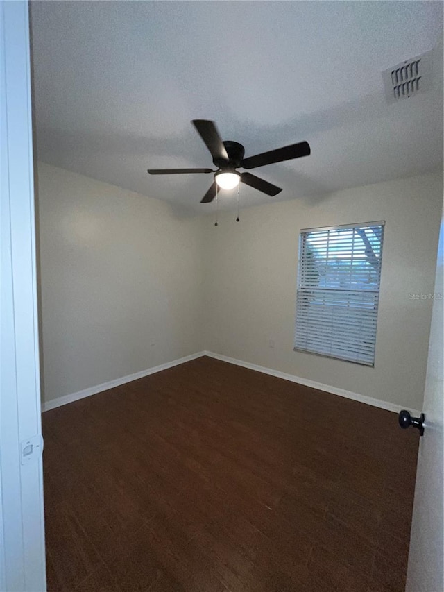 empty room featuring dark wood-style floors, visible vents, baseboards, and a ceiling fan