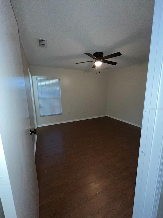 spare room featuring visible vents, dark wood finished floors, baseboards, and ceiling fan