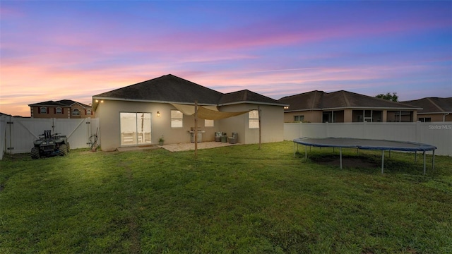 rear view of house featuring a fenced backyard, a lawn, a gate, stucco siding, and a trampoline