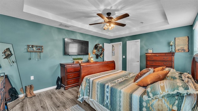 bedroom with wood finished floors, a ceiling fan, visible vents, baseboards, and a raised ceiling