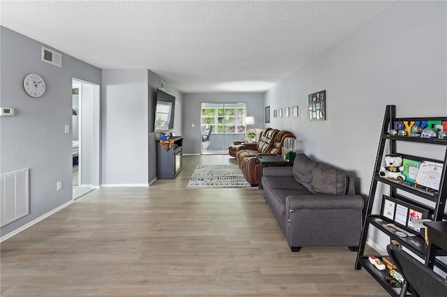 living area featuring a textured ceiling, wood finished floors, visible vents, and baseboards