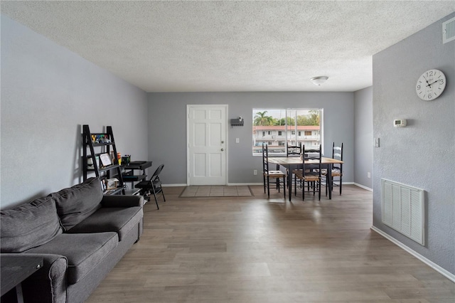 living area featuring baseboards, a textured ceiling, visible vents, and wood finished floors